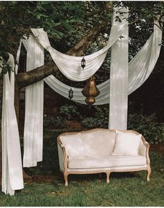 a white couch sitting under a tree next to a canopy covered in draping