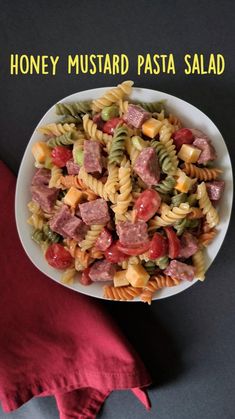 a white bowl filled with pasta salad on top of a red cloth next to a napkin