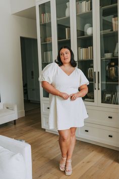 a woman in a white dress standing in front of a bookcase with books on it