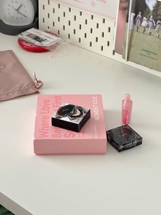 a pink box sitting on top of a white desk next to a watch and lipstick