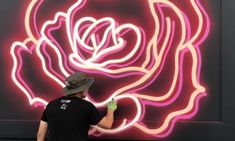 a man painting a rose on the side of a building with neon lights behind him