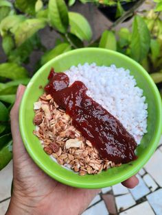 a person holding a green bowl filled with rice and jelly on top of granola