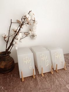 three small white cards with gold numbers are sitting on a table next to a cotton plant