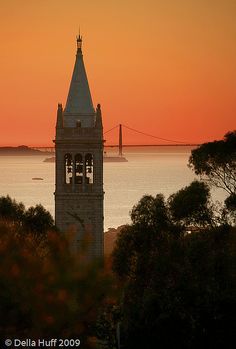 the sun is setting behind a tower with a clock on it's side and water in the background