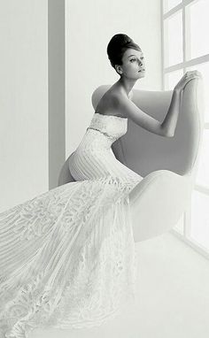 a woman in a white dress sitting on a couch next to a window and looking out the window