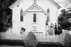 a black and white photo of people standing in front of a church with picket fence