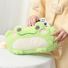 a person holding a green stuffed animal on top of a white tablecloth with a remote control in it's hand