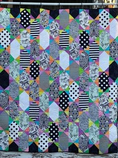 a colorful quilt hanging on the side of a fence with polka dots and black and white stripes