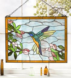 a stained glass window with a hummingbird and flowers hanging from it's side