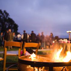 an outdoor fire pit with people sitting around it at dusk or dawn, in the evening