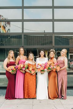 a group of women standing next to each other in front of a glass building holding bouquets