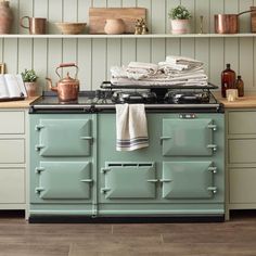 a green stove top oven sitting inside of a kitchen next to wooden shelves and pots