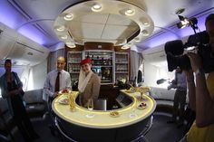 a man standing in front of a bar on an airplane with people around him taking pictures