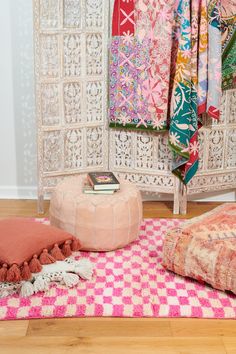 a pink and white area rug on the floor next to a bed with pillows, blankets and books