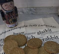 some cookies are sitting on a newspaper next to a cup and canister with the word celebration of the scots