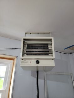 an air conditioner sitting on top of a white wall in a room with windows