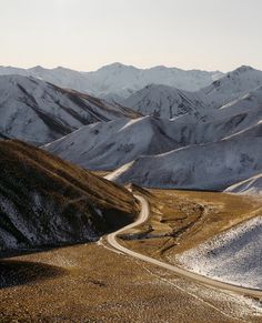 the mountains are covered in snow and there is a winding road going through one side