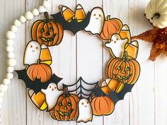 a wreath made out of paper with pumpkins and ghost faces on it next to a white bead necklace