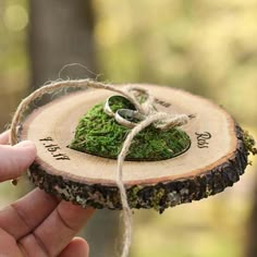 a hand holding a piece of wood with moss on it and two wedding rings tied to the end