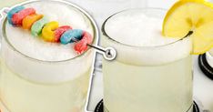 two glasses filled with white liquid next to lemon slices and candy worms on the rim