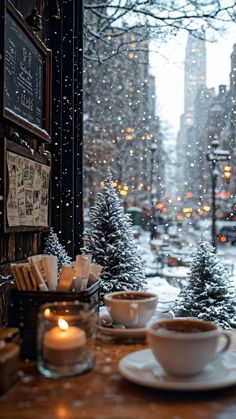 two cups and saucers on a table in front of a window with snow falling