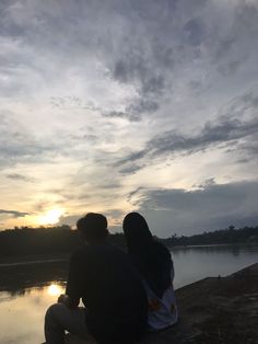 two people sitting on the edge of a body of water watching the sun go down