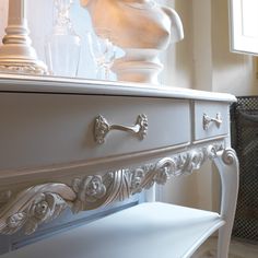 an ornate white dresser with glass vases on top