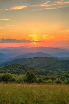 the sun is setting over the mountains in the distance, and there are trees on the far side