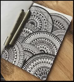 an open notebook with black and white doodles on it, next to a pen