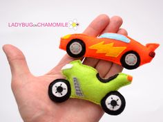 a hand holding two small toy cars in each other's palm, one is orange and the other is green