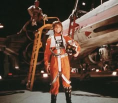 a man in an orange space suit standing next to a plane