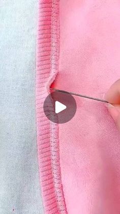 someone is using scissors to cut the side of a pink sweater with white trims