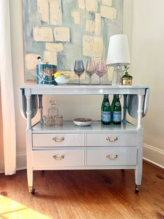 a table with two wine glasses and bottles on it in front of a large painting