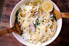 a white bowl filled with pasta and meat on top of a wooden table next to a cutting board