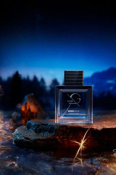 a bottle of perfume sitting on top of a rock next to water and trees at night