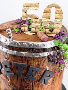 a birthday cake decorated with wine corks and grapes is displayed on a wooden barrel