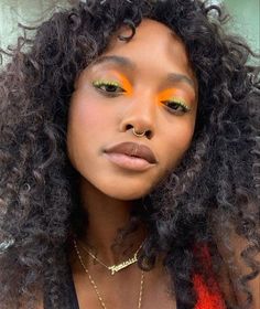 a woman with bright orange eyeshadow and long curly hair is looking at the camera