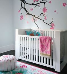 a white crib with pink flowers and a tree branch painted on the wall behind it