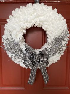 a wreath is hanging on the front door with white yarn and black plaid ribbon around it