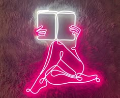 a neon sign with a person reading a book on it's head and legs