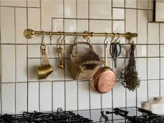 pots and pans are hanging on the wall above the stove in this white tiled kitchen