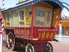 a red and yellow horse drawn carriage in front of an amusement park ride at the theme park