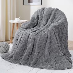 a large gray blanket sitting on top of a bed next to a white table and chair