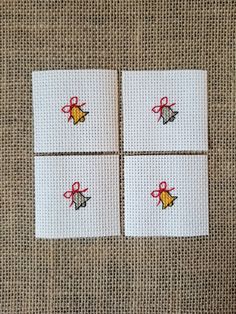 four cross stitch coasters with bows and bells on white fabric, set of 4