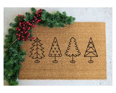 a door mat with trees drawn on it next to evergreen branches and red berry berries