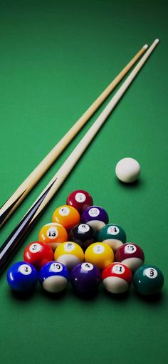 billiards and pool balls on a green table with cues in the foreground