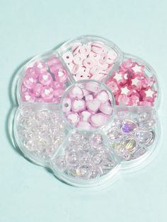 there are many different beads in the container on the blue table top, including pink and white ones