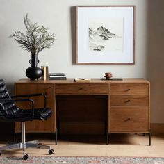 a desk with a chair and vase on top of it next to a framed mountain scene