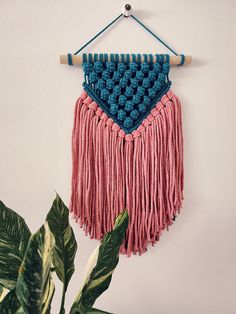 a pink and blue wall hanging next to a potted plant