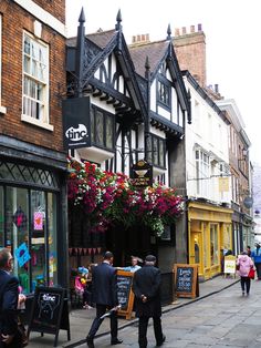 two men in suits are walking down the street with flowers hanging over their heads and windows